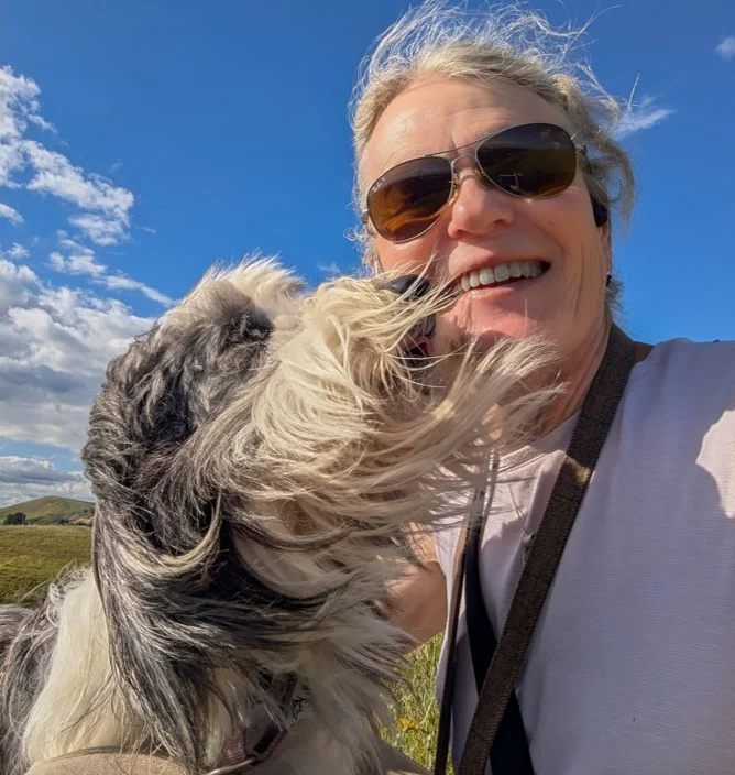 Rebecca Lewington on a trail with her dog, blue sky and green hills behind